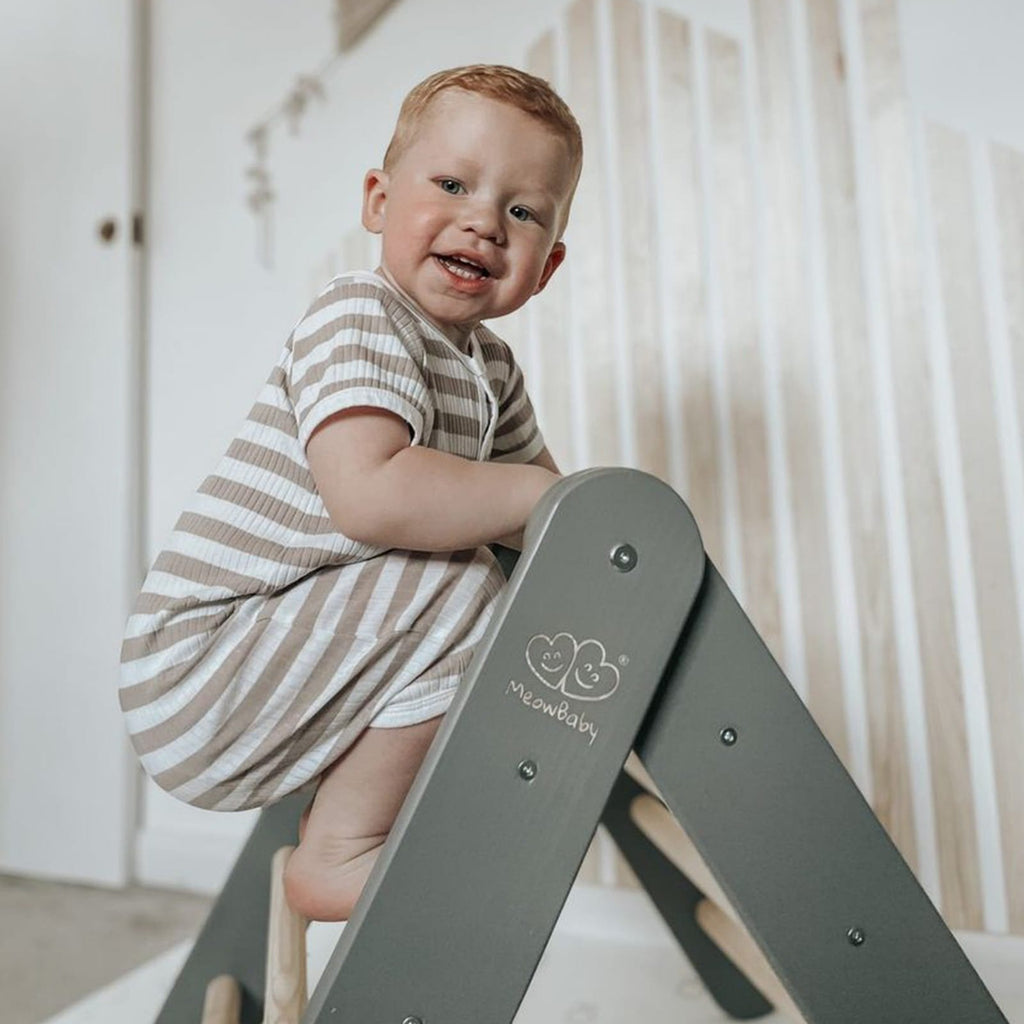 1. Child climbing grey wooden ladder structure in playroom, smiling and engaging in play