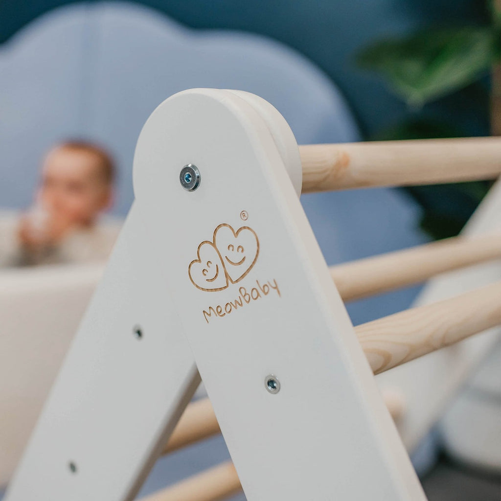 3. Close-up of MeowBaby logo on white wooden Pikler ladder with blurred child in background