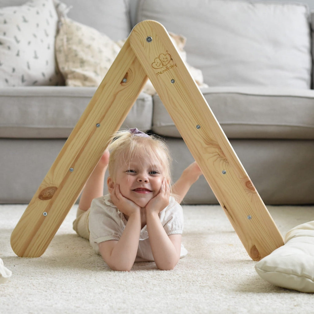 15. Child lying under natural wood ladder in a living room, smiling and engaging with the play structure