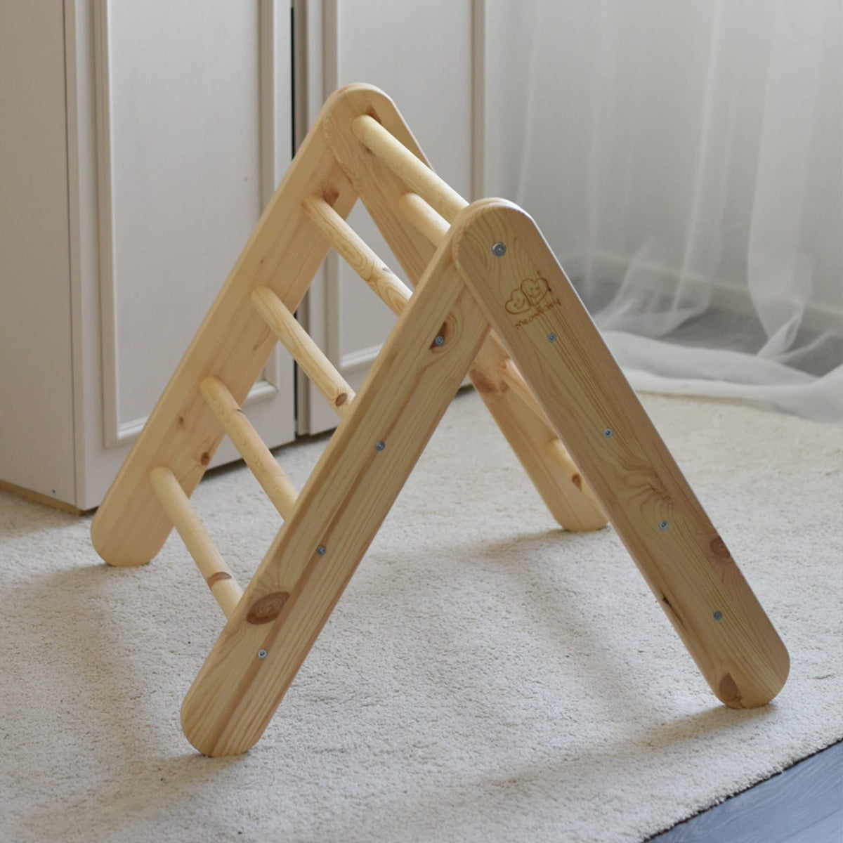 5. Wooden Pikler climbing ladder in natural wood on a carpeted floor, near a window with curtains.