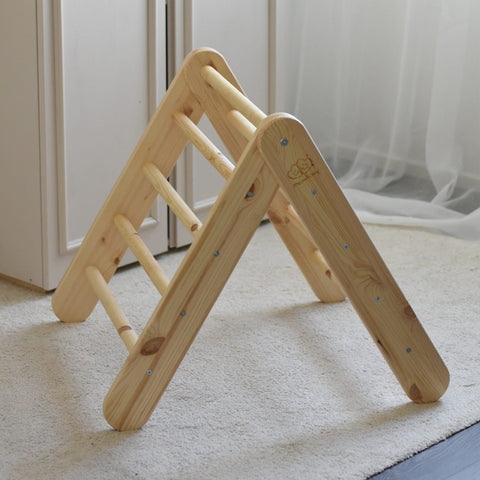 5. Wooden Pikler climbing ladder in natural wood on a carpeted floor, near a window with curtains.