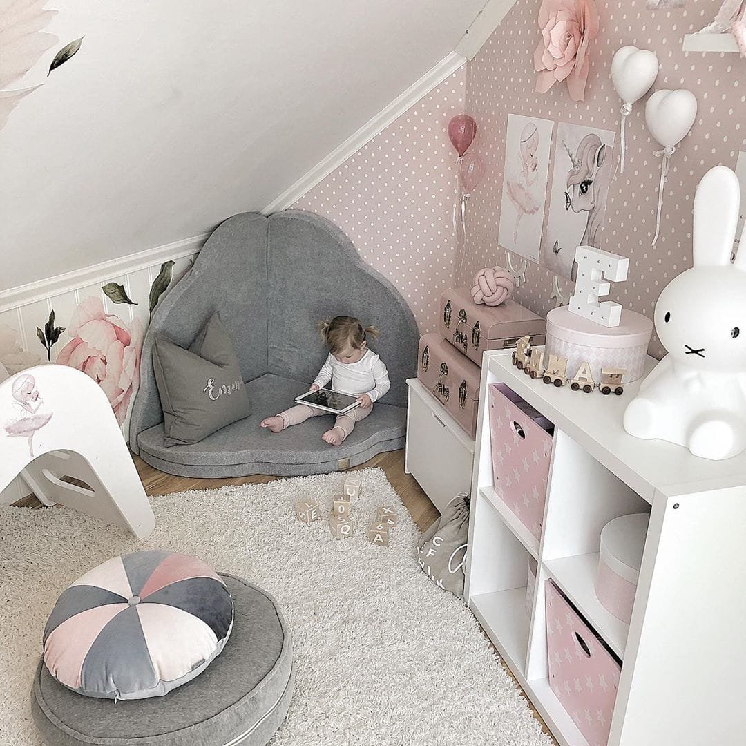 4. Child reading on light grey cloud-shaped play mat in pink-themed playroom