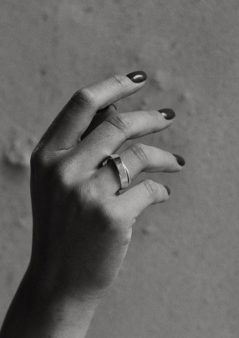 1. Black and white image of a woman's hand wearing the Milky Way ring by NO MORE, with a textured wall background