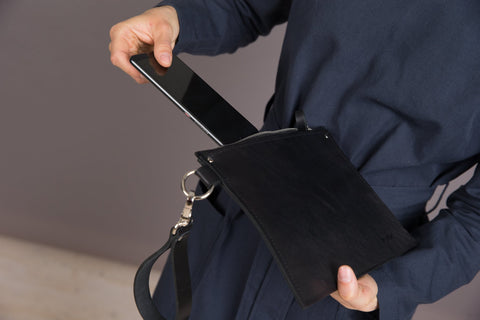 3. Close-up of woman placing a phone into black leather Clutch Nina by PYKOK, showing wrist strap and zipper
