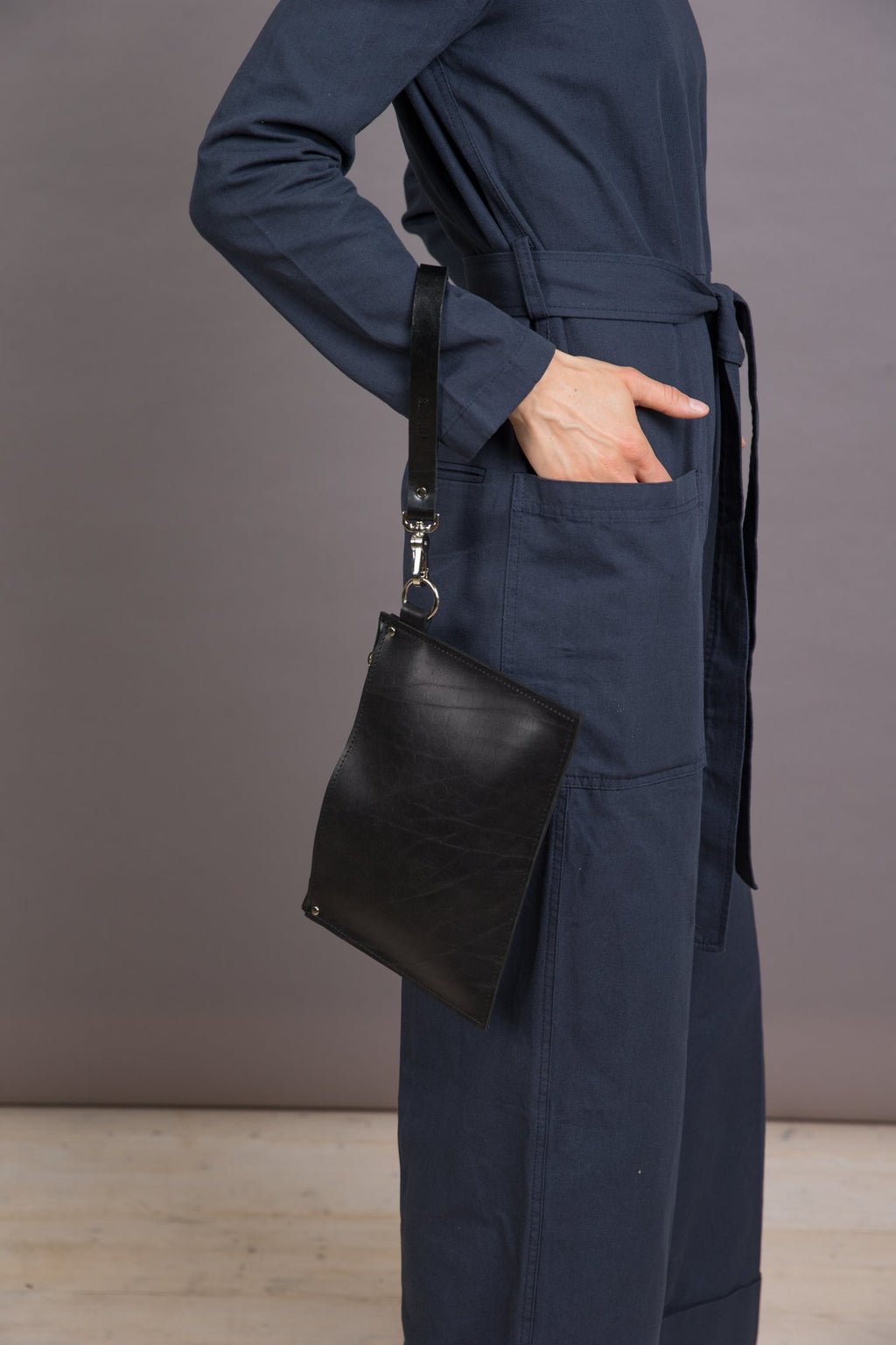 2. Woman wearing black leather Clutch Nina by PYKOK with wrist strap, styled with a navy outfit