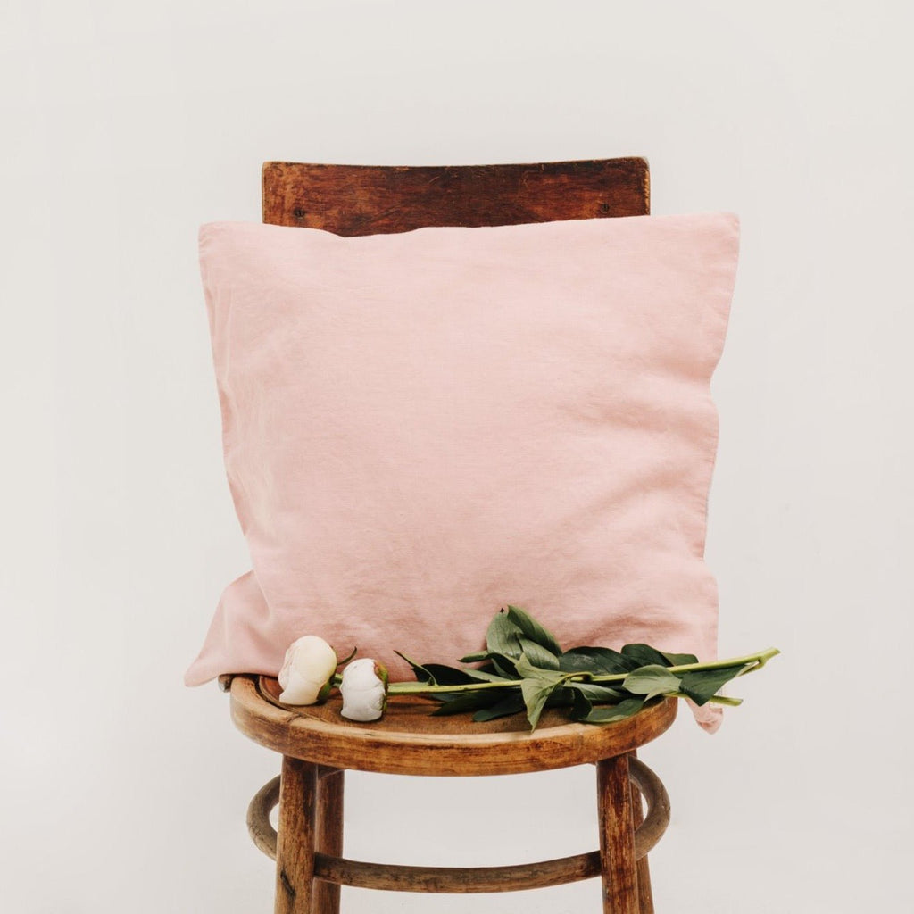5. Misty rose Linen Tales cushion cover on a wooden chair with green leaves and white flowers