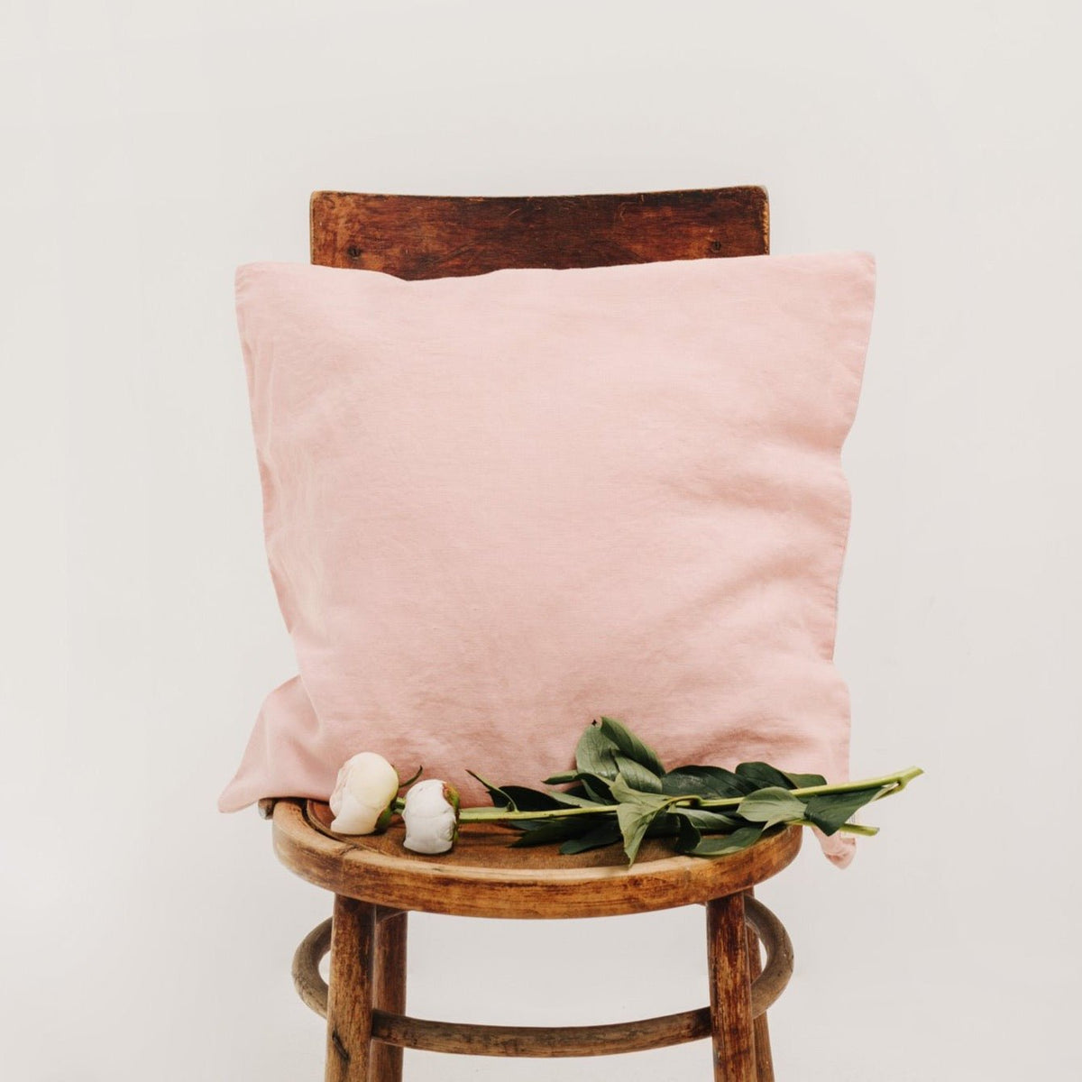5. Misty rose Linen Tales cushion cover on a wooden chair with green leaves and white flowers