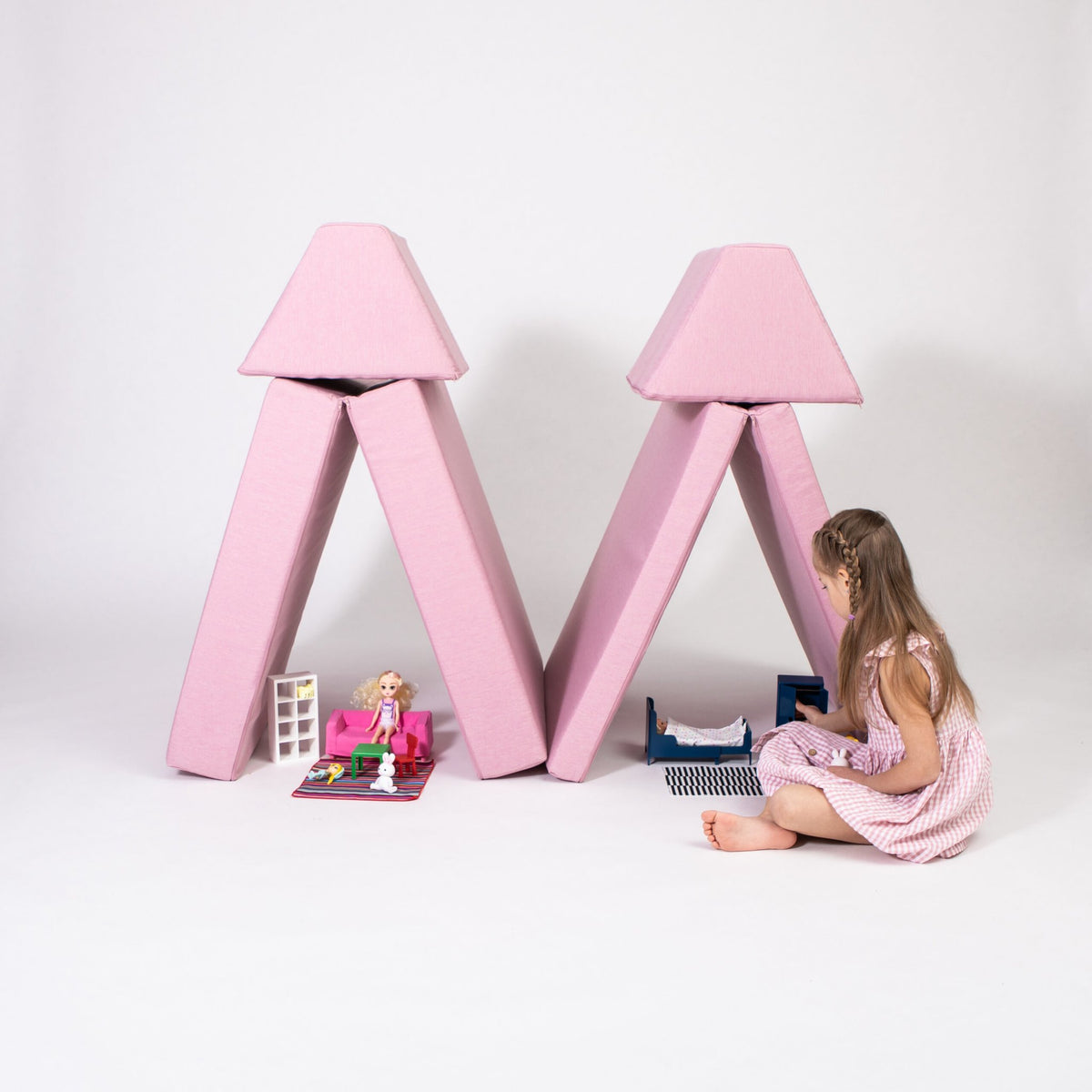1. Girl playing with pink play mattress set arranged as tents on a white background