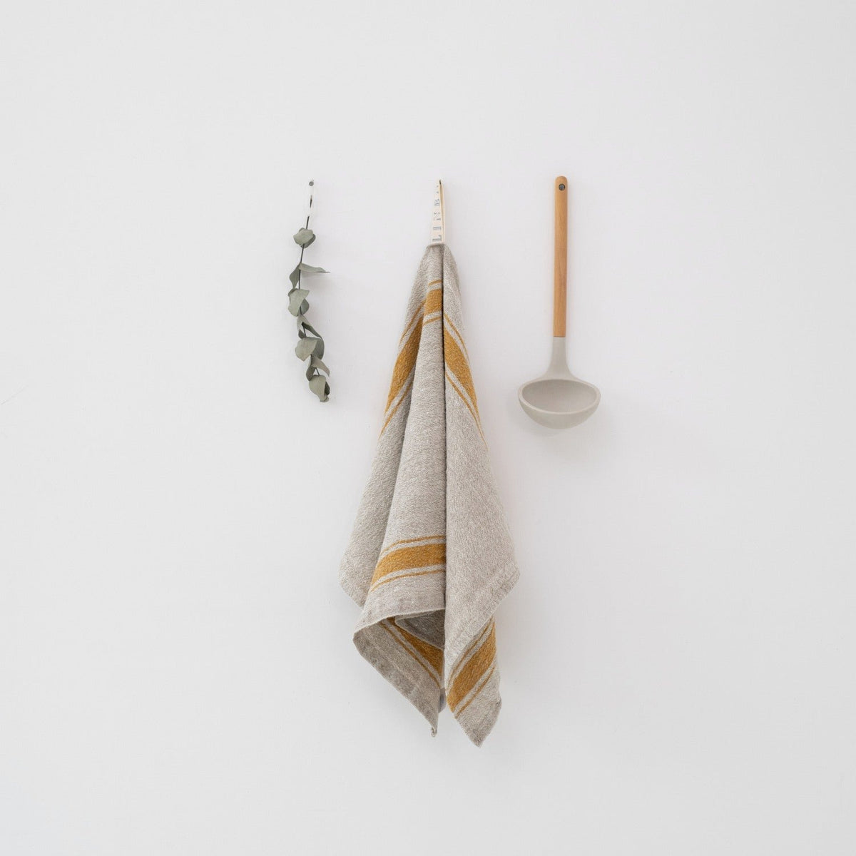 3. Beige linen kitchen towel with mustard stripes hanging on white wall with ladle