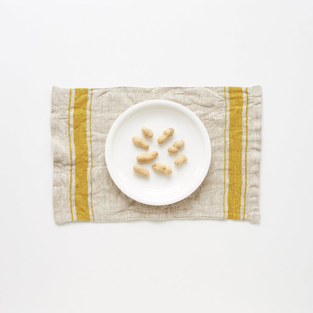 3. Mustard vintage stripe linen placemat with a white plate and peanuts on a white background