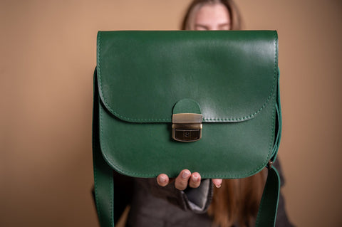 2. Woman holding Zelma Kraft green leather saddle bag, highlighting semi-gloss finish and buckle detail
