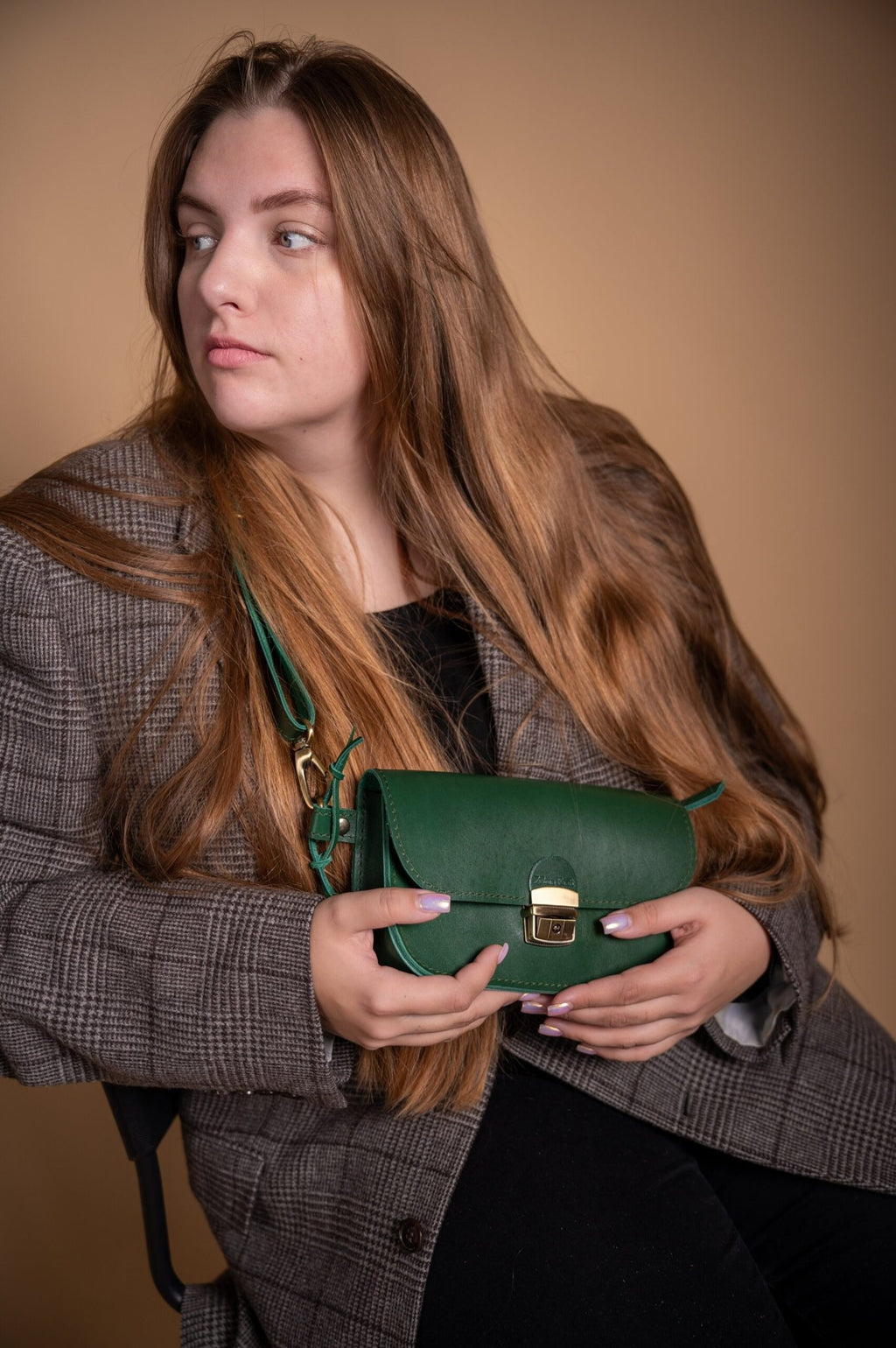 1. Woman holding Zelma Kraft green leather saddle bag mini, styled with a plaid blazer in a lifestyle setting
