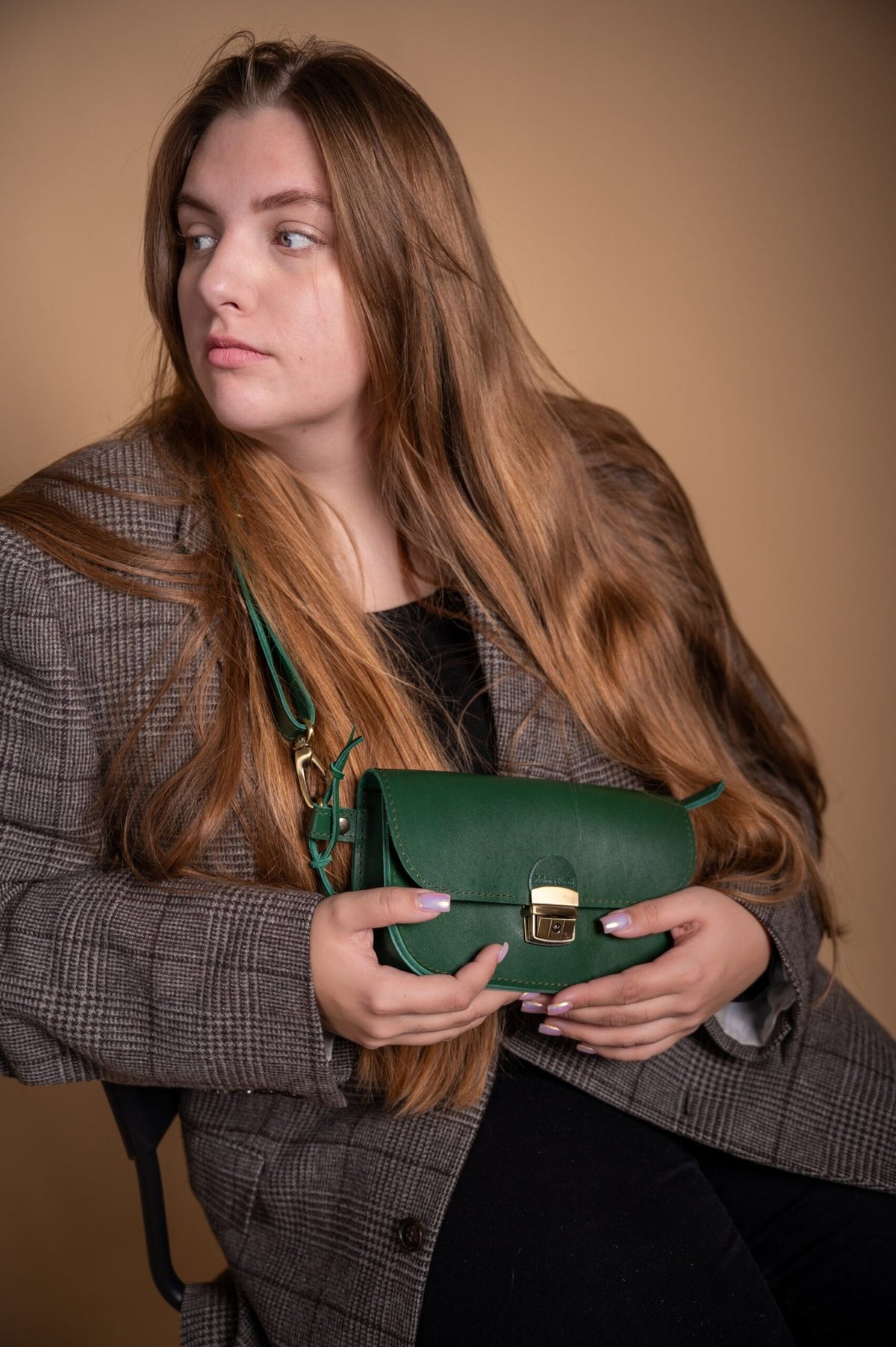1. Woman holding Zelma Kraft green leather saddle bag mini, styled with a plaid blazer in a lifestyle setting