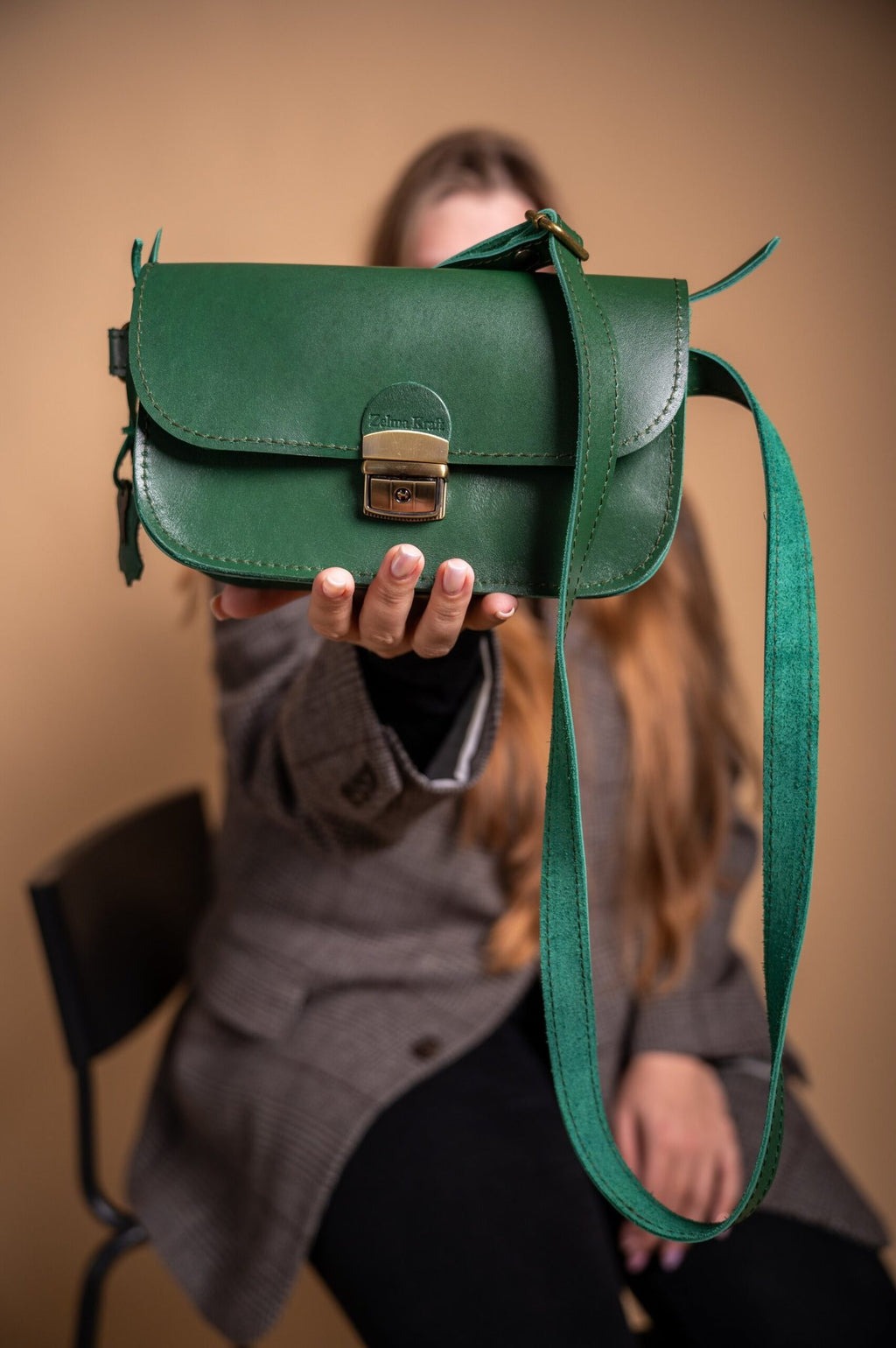 2. Woman presenting Zelma Kraft green leather saddle bag mini, showcasing adjustable strap and buckle closure