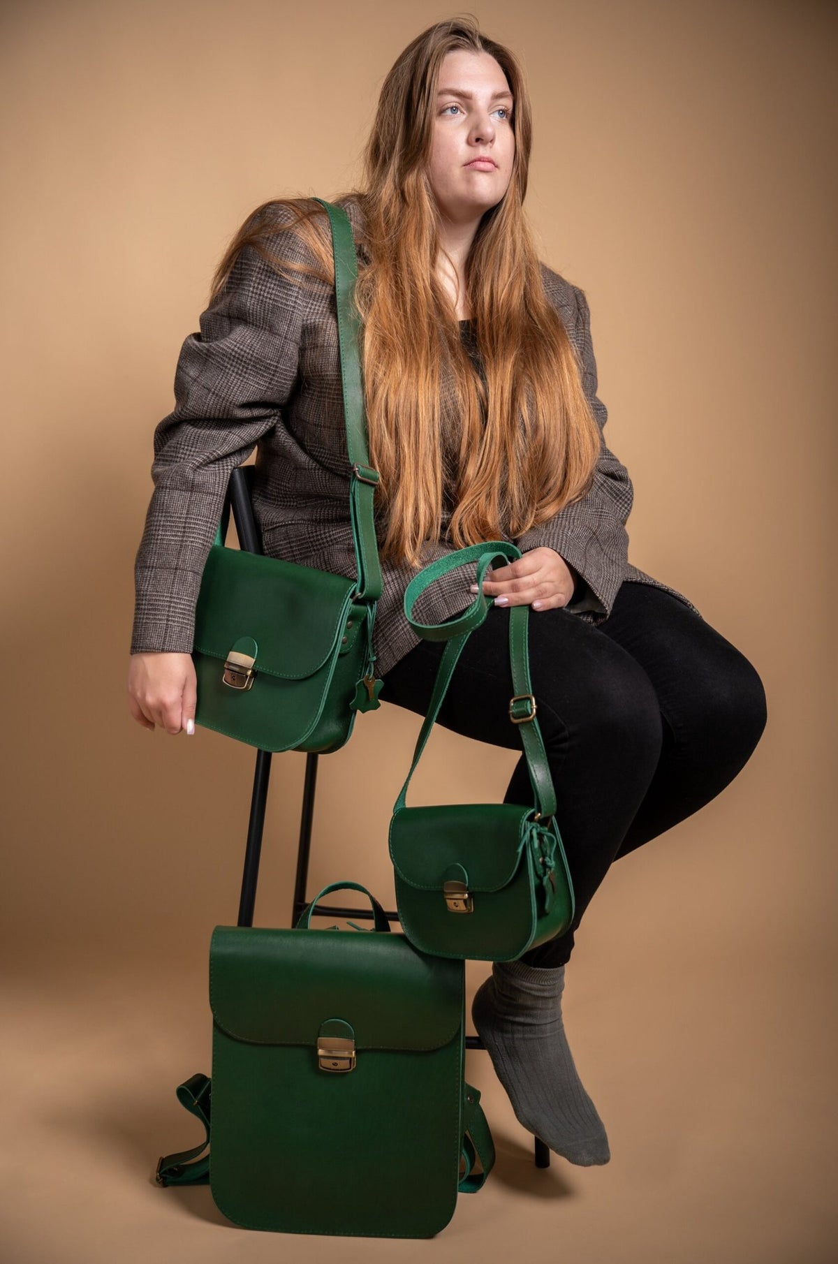 2. Woman seated with Zelma Kraft green leather saddle backpack and matching accessories in lifestyle setting