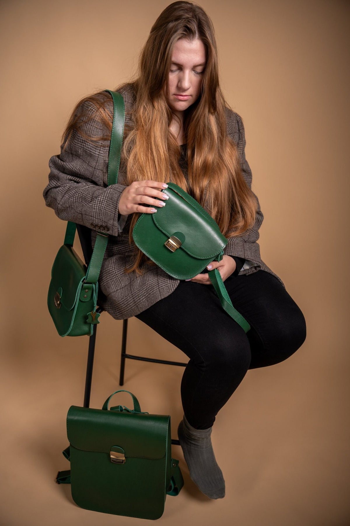 1. Woman sitting with Zelma Kraft green leather saddle bag, showcasing adjustable strap and buckle closure