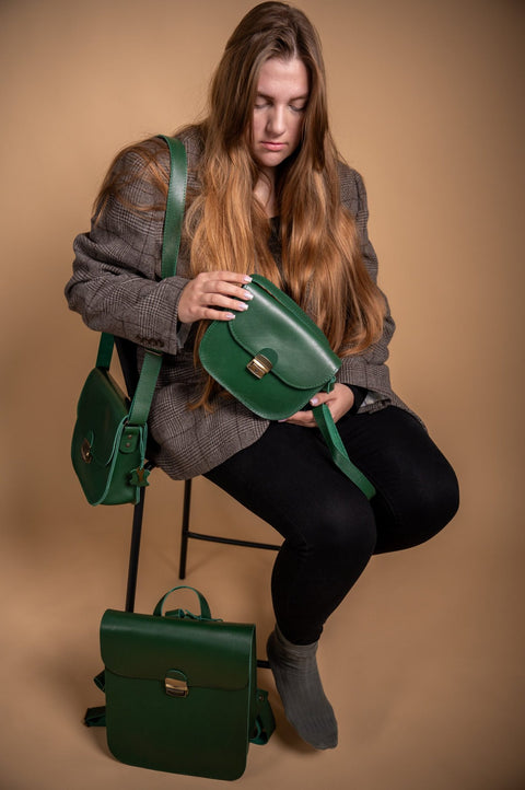 1. Woman sitting with Zelma Kraft green leather saddle bag, showcasing adjustable strap and buckle closure