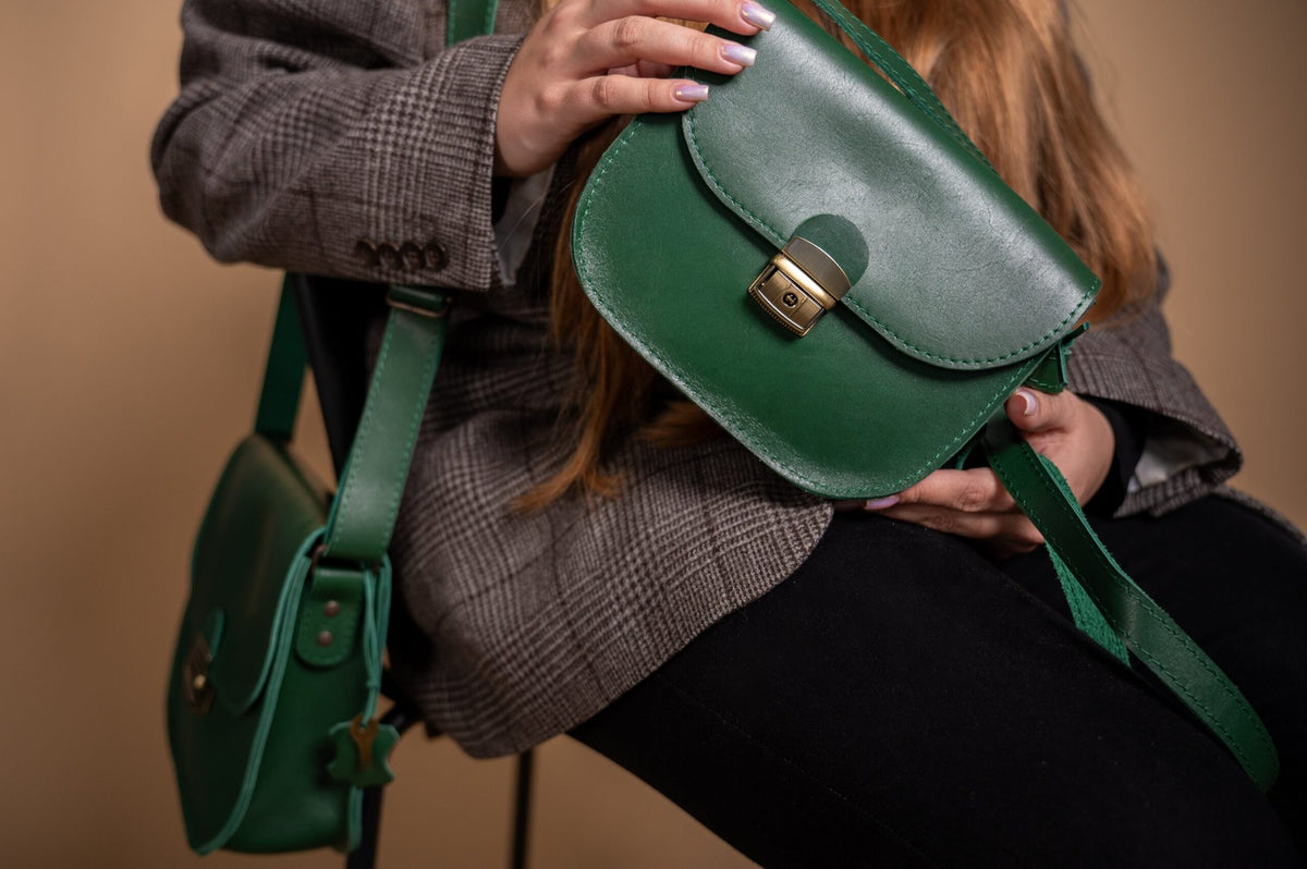 1. Woman holding Zelma Kraft green leather saddle bag with adjustable strap, styled with a plaid blazer