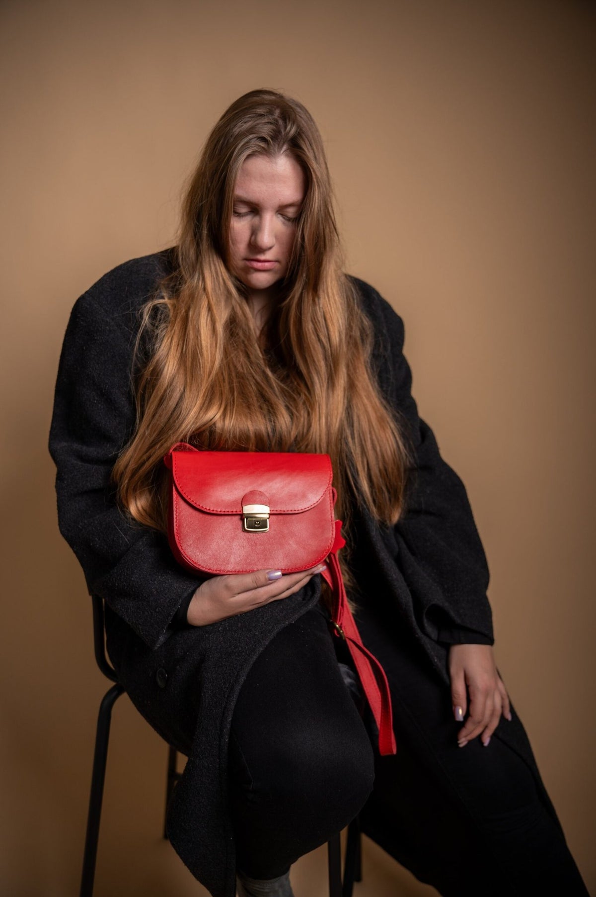 1. Woman holding Zelma Kraft red natural leather saddle bag, showcasing its elegant design in a lifestyle setting