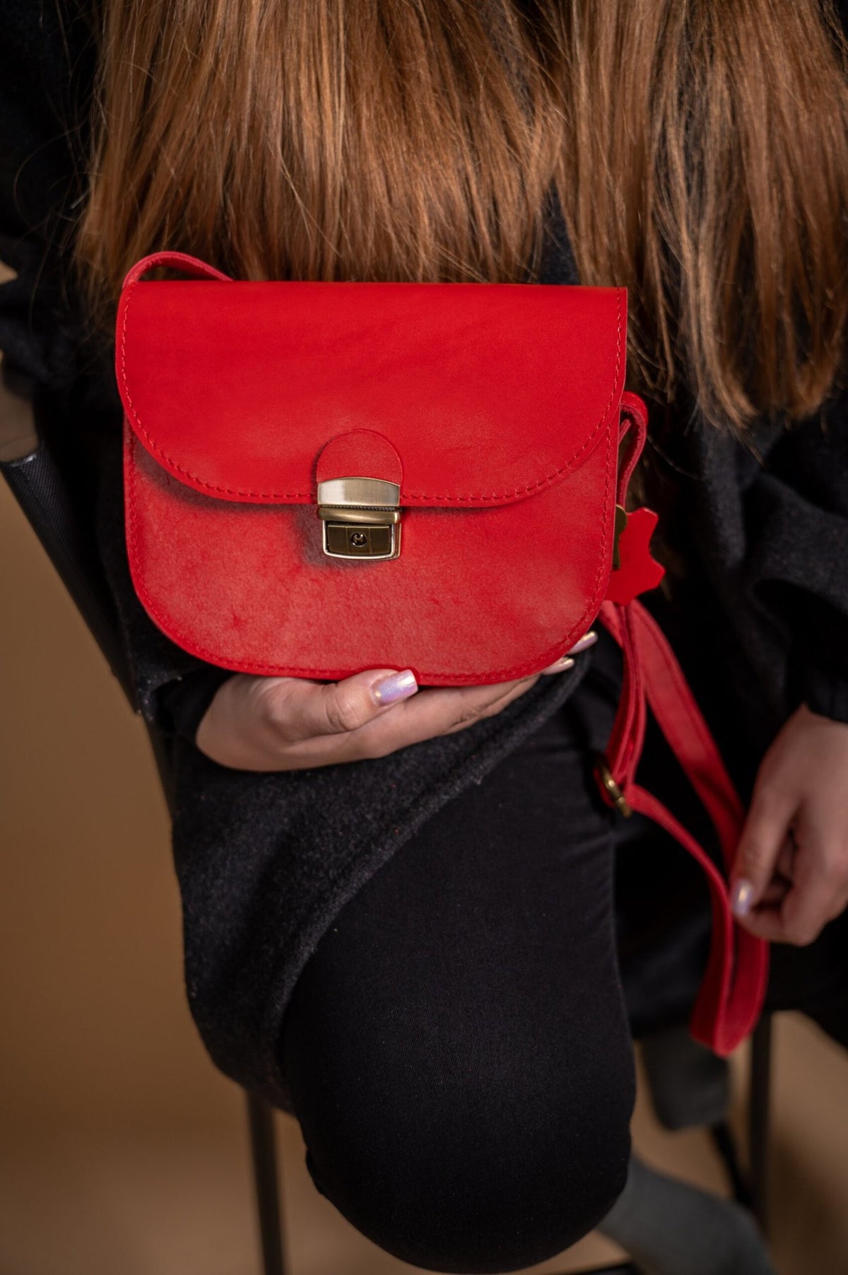 3. Close-up of woman holding Zelma Kraft red leather saddle bag, emphasizing its semi-gloss finish and buckle closure