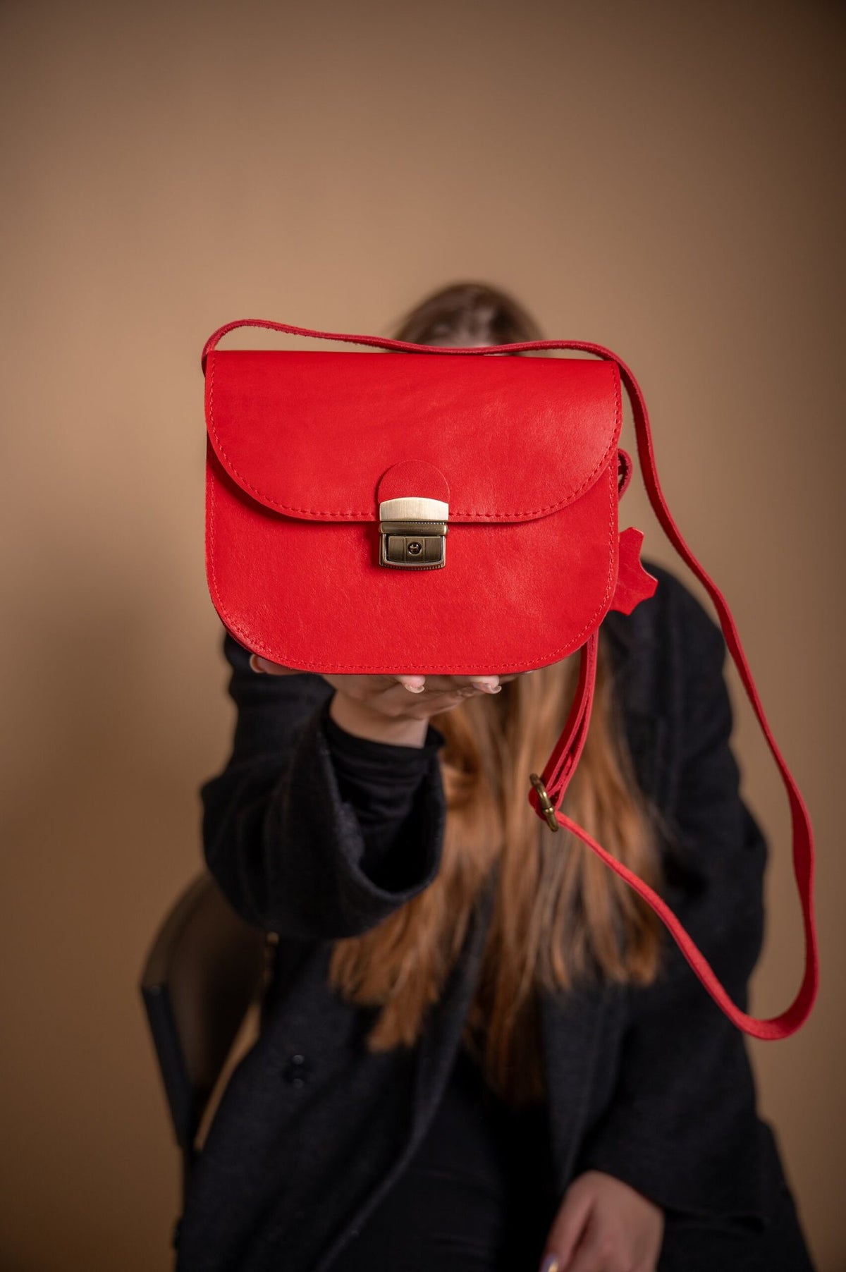 2. Woman presenting Zelma Kraft red leather saddle bag, highlighting its stylish appearance and adjustable strap