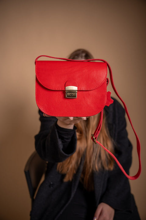 2. Woman presenting Zelma Kraft red leather saddle bag, highlighting its stylish appearance and adjustable strap