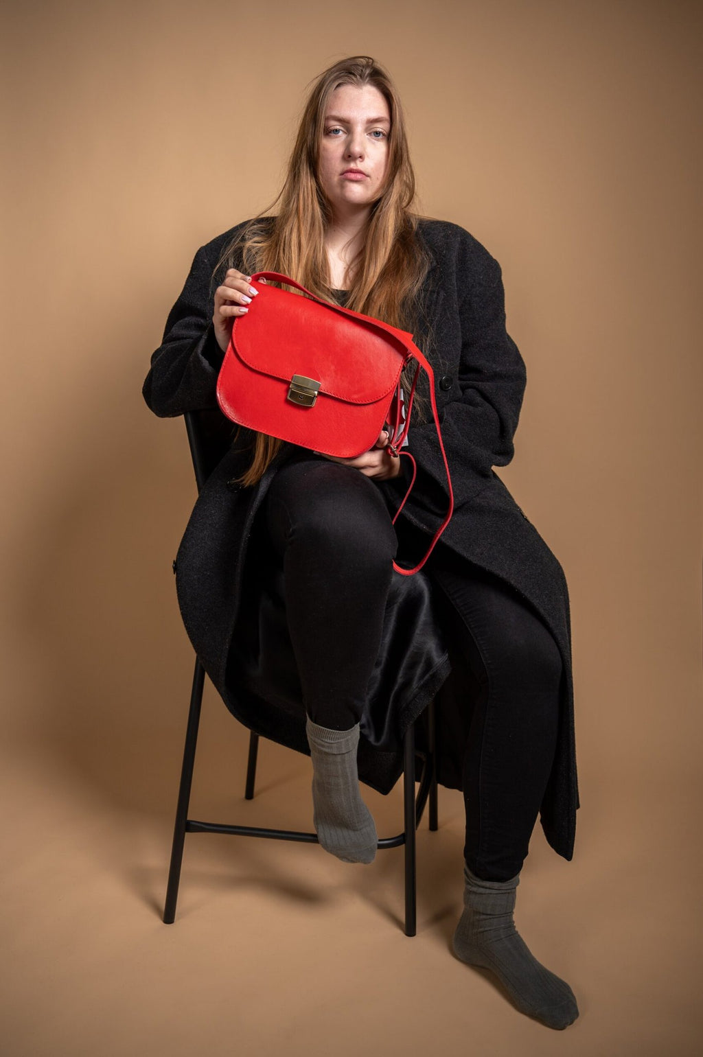 1. Woman holding Zelma Kraft red natural leather saddle bag, showcasing its size and style in a lifestyle setting