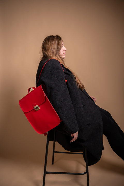 1. Woman wearing Zelma Kraft red leather saddle backpack, styled with a black coat, sitting in a studio setting