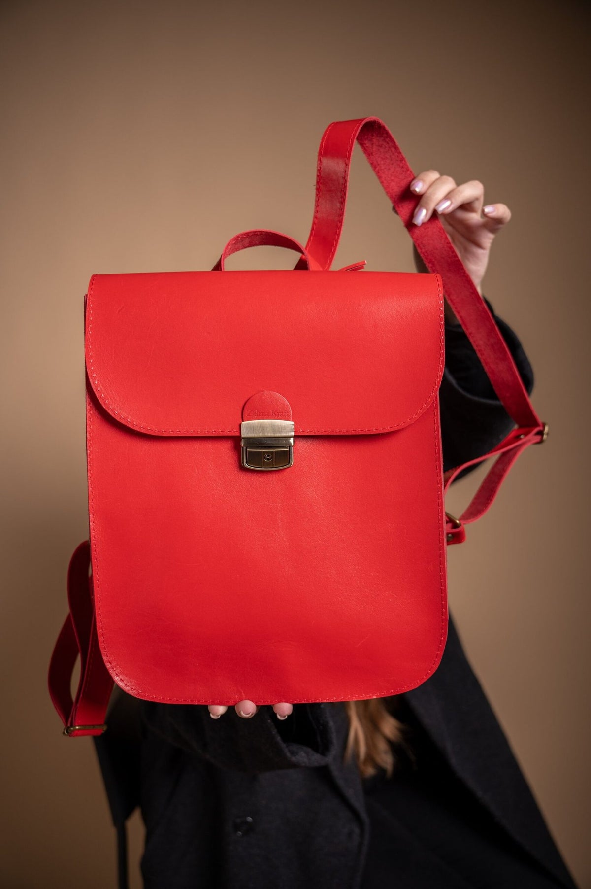 4. Zelma Kraft red leather saddle backpack held by a woman, showcasing adjustable straps and minimalist design