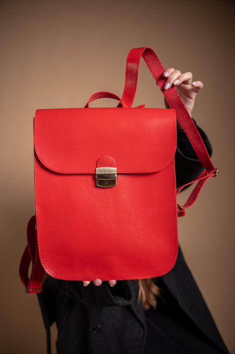 4. Zelma Kraft red leather saddle backpack held by a woman, showcasing adjustable straps and minimalist design