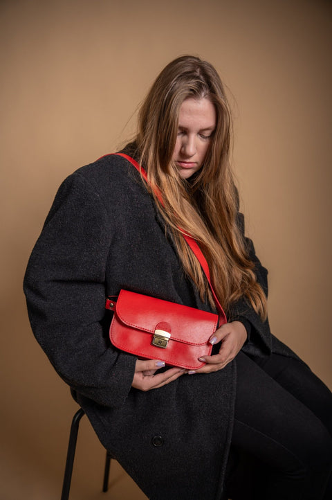 2. Woman wearing Zelma Kraft red leather saddle bag, styled with black coat in lifestyle setting