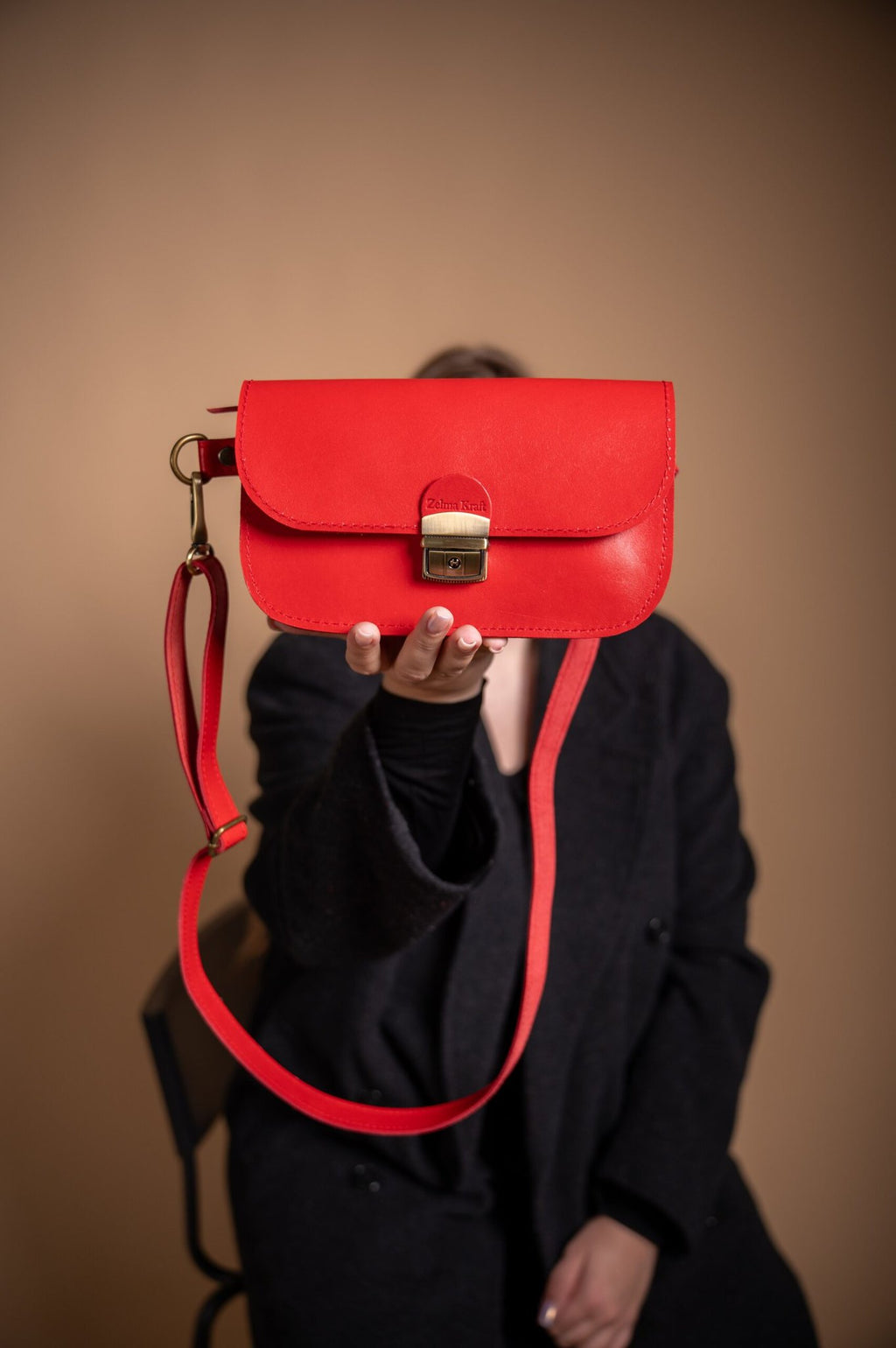 3. Red leather saddle bag by Zelma Kraft held by model, showcasing buckle closure and adjustable strap