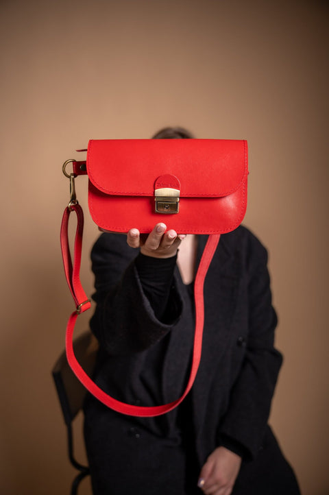 3. Red leather saddle bag by Zelma Kraft held by model, showcasing buckle closure and adjustable strap