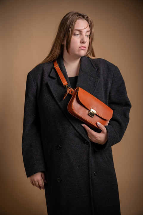 1. Woman wearing Zelma Kraft natural leather saddle bag mini in light brown, styled with a black coat