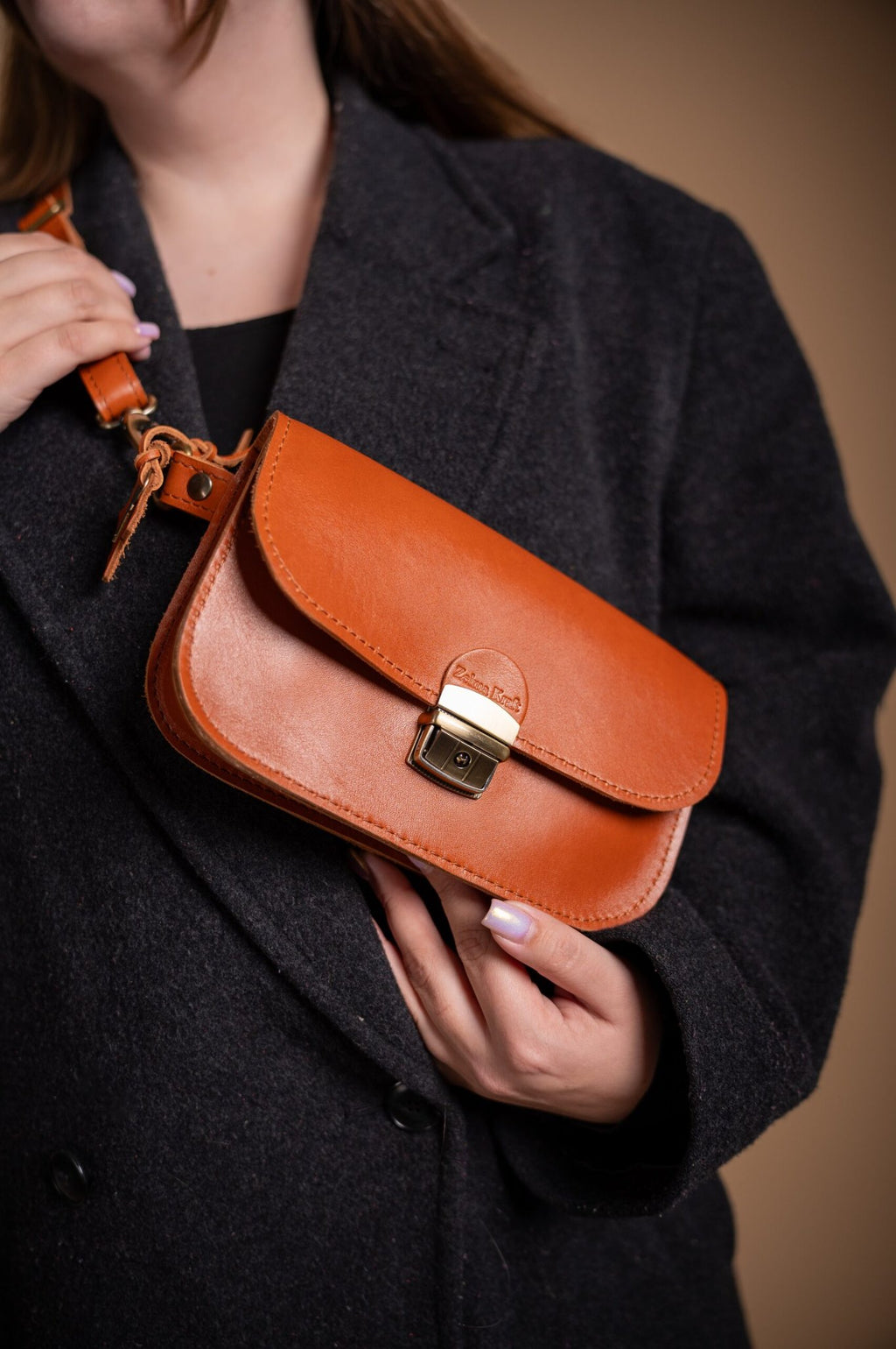 2. Woman holding Zelma Kraft natural leather saddle bag mini in light brown, shown with adjustable strap