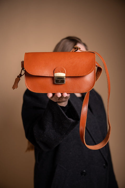 3. Woman presenting Zelma Kraft natural leather saddle bag mini in light brown, highlighting buckle closure
