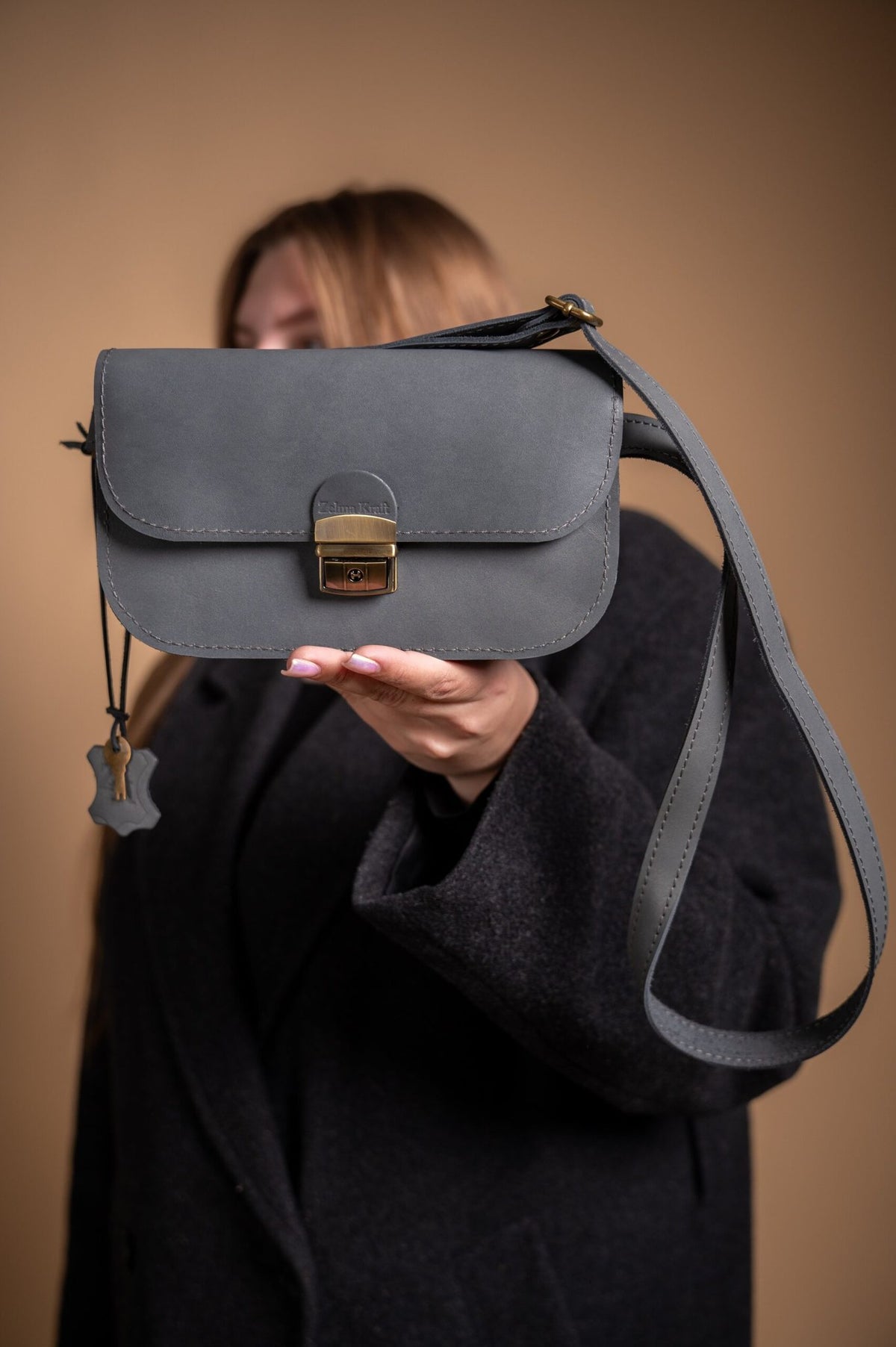 6. Woman holding grey leather saddle bag mini by Zelma Kraft, showing adjustable strap and compact design