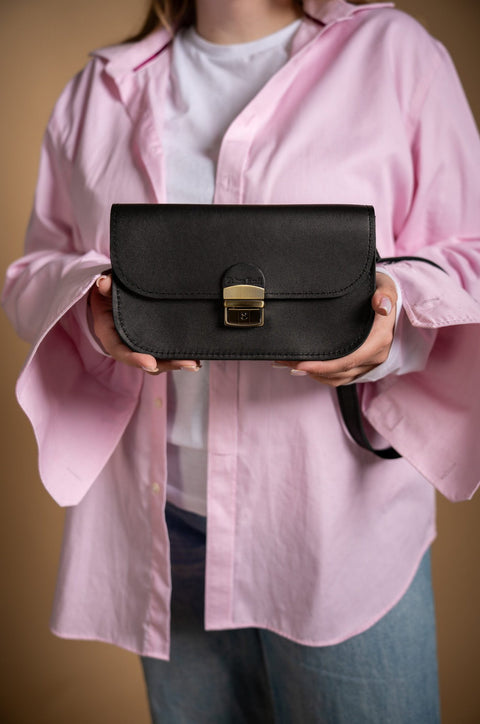1. Women's black Zelma Kraft natural leather saddle bag mini held by model in pink shirt