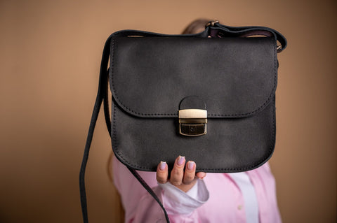 4. Woman displaying Zelma Kraft black leather saddle bag against a neutral background