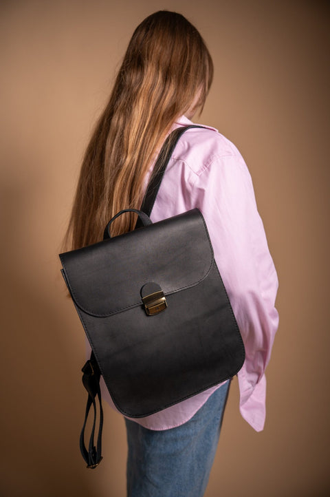 1. Woman wearing Zelma Kraft black leather saddle backpack, shown from the back in lifestyle setting
