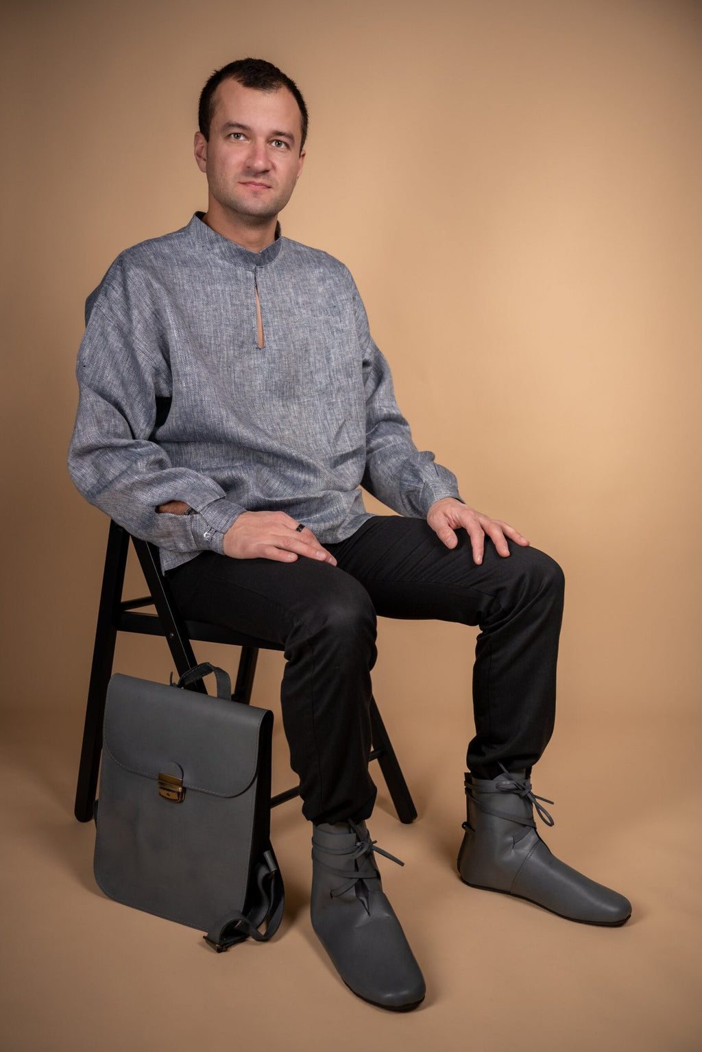 1. Men's grey Zelma Kraft leather saddle backpack styled with matching outfit, shown in lifestyle setting