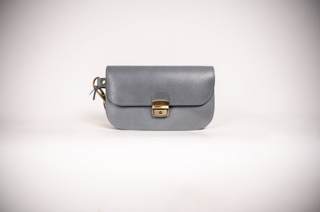 3. Studio image of grey natural leather saddle bag mini by Zelma Kraft, featuring buckle closure and compact design