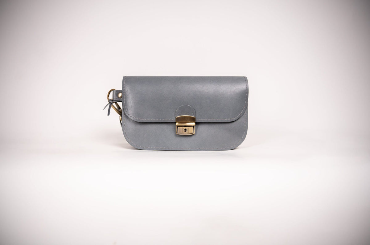 3. Studio image of grey natural leather saddle bag mini by Zelma Kraft, featuring buckle closure and compact design