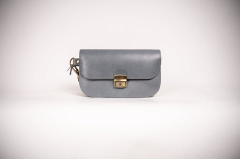 3. Studio image of grey natural leather saddle bag mini by Zelma Kraft, featuring buckle closure and compact design