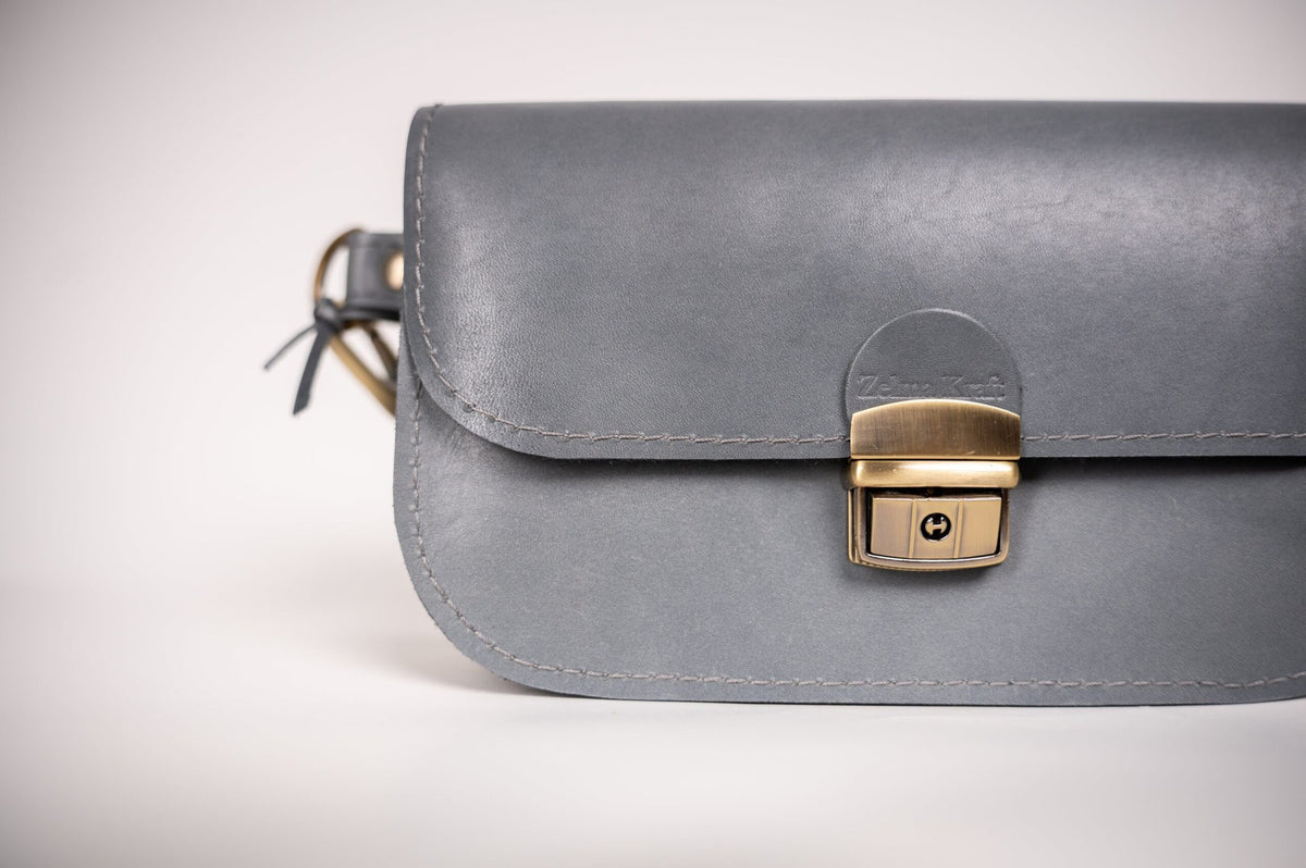 5. Close-up of grey leather saddle bag mini by Zelma Kraft, highlighting buckle closure and semi-glossy finish