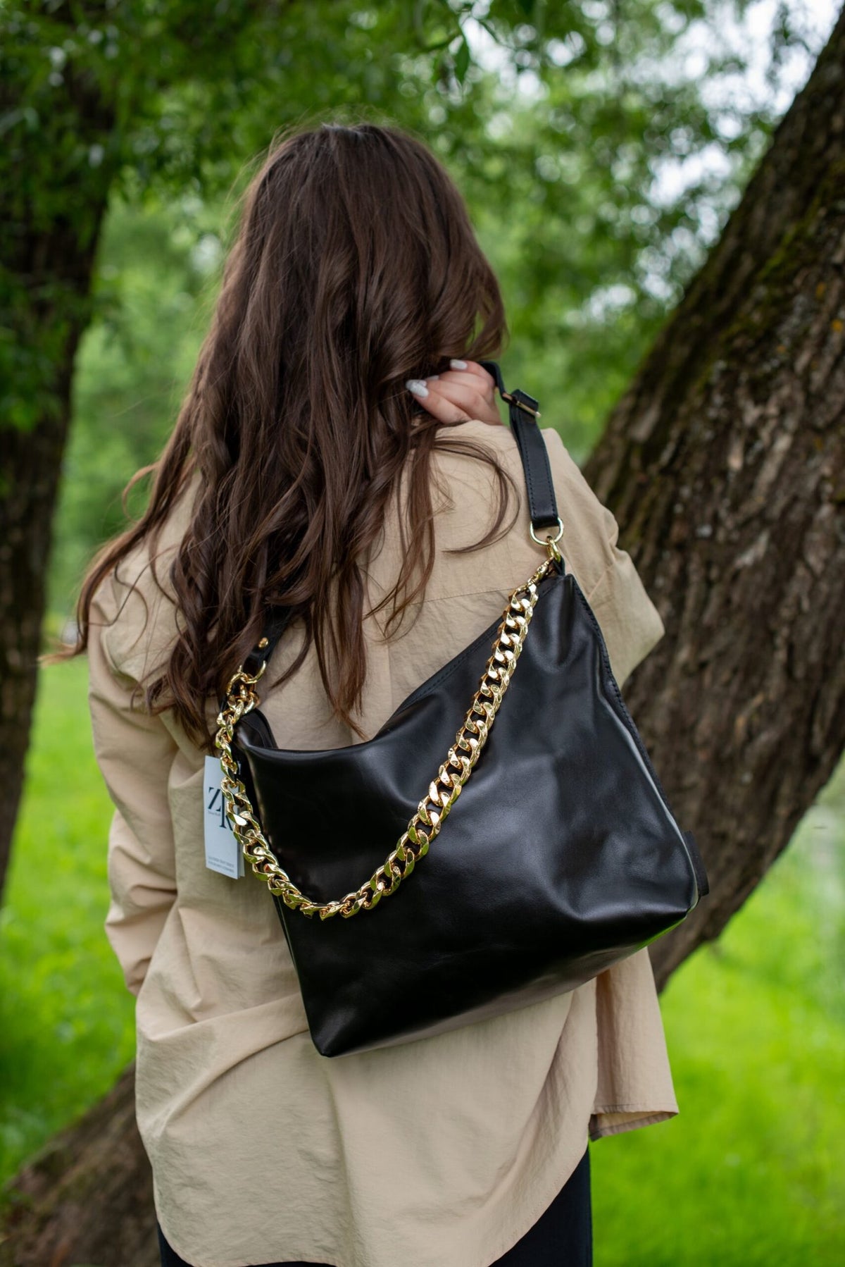 3. Woman wearing Zelma Kraft black leather hobo bag with gold chain strap, shown from the side