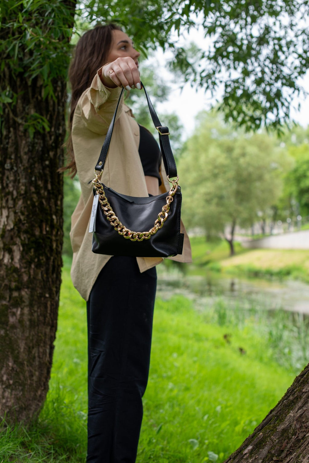 1. Woman holding Zelma Kraft black leather hobo bag with gold chain in outdoor setting