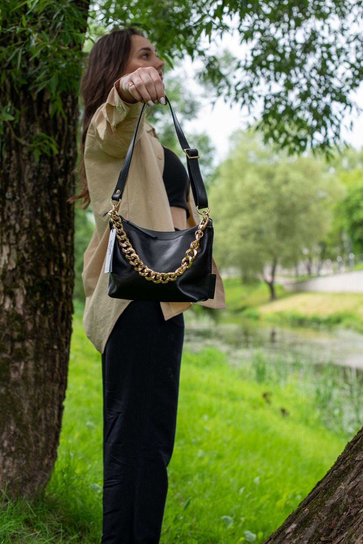 1. Woman holding Zelma Kraft black leather hobo bag with gold chain in outdoor setting