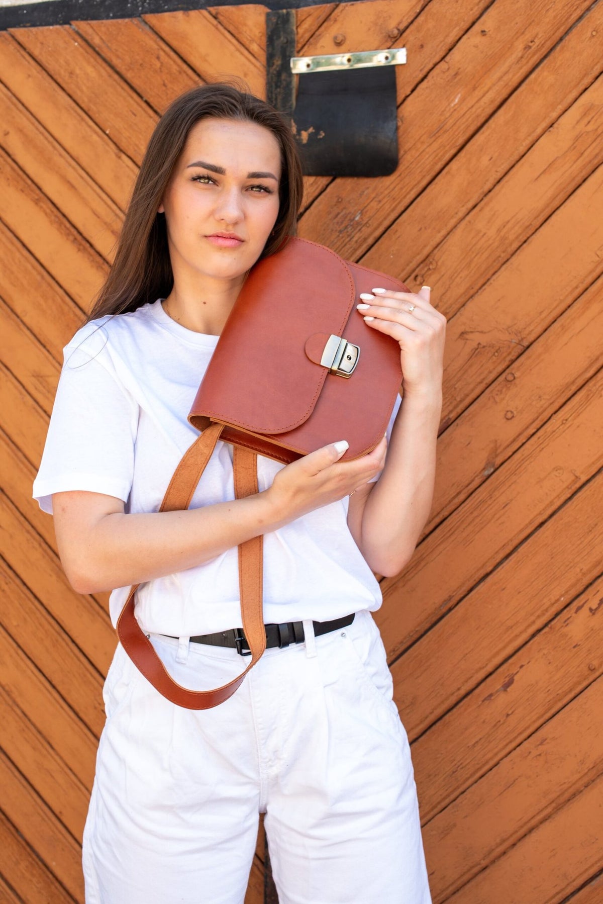1. Woman holding Zelma Kraft natural leather saddle bag in light brown, showcasing adjustable strap and buckle closure