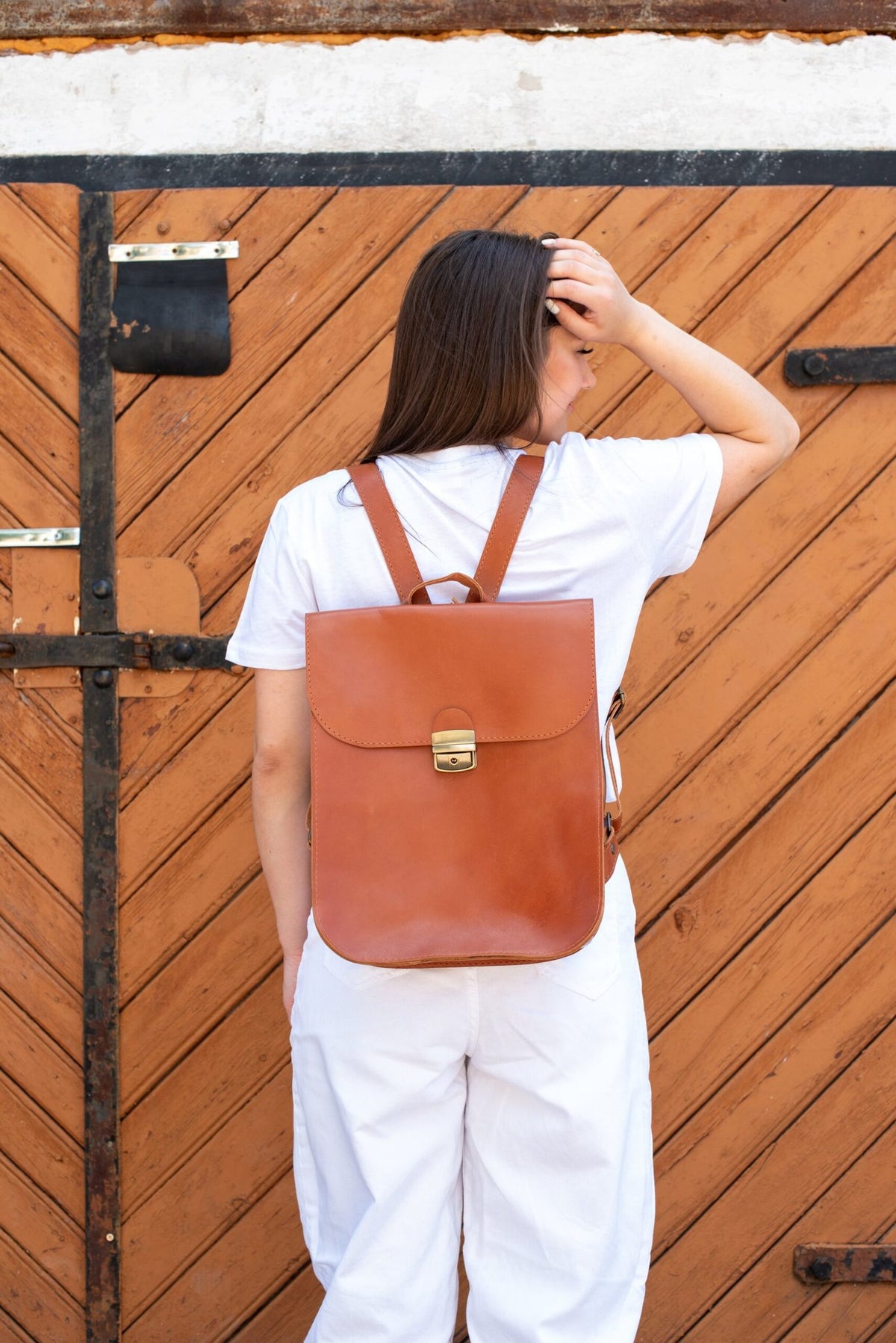 1. Woman wearing Zelma Kraft natural leather saddle backpack in light brown, shown from the back in a lifestyle setting
